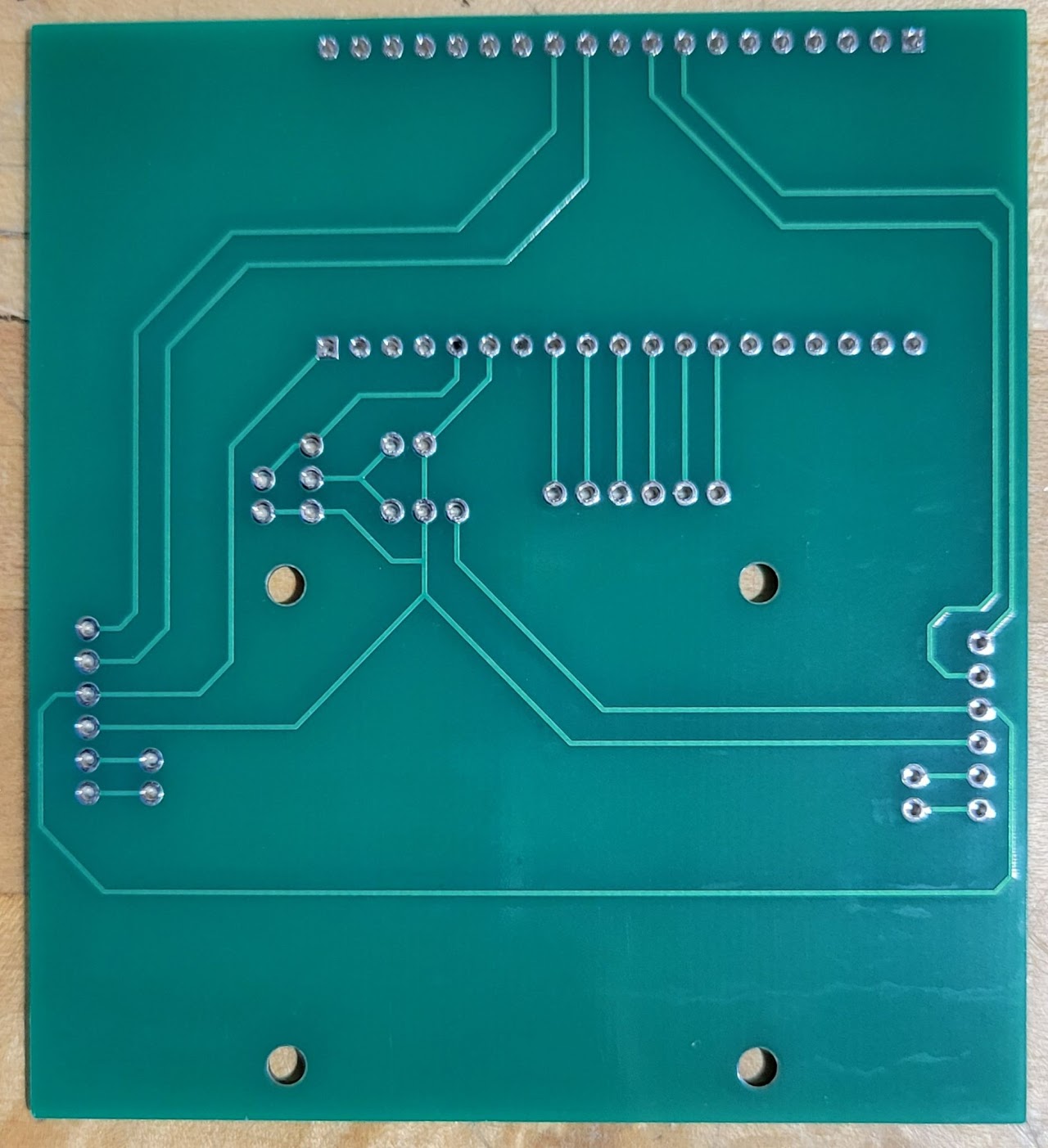 A small PCB with through-holes for a microcontroller, several pin headers, and some resistors, as well as four mounting holes for the motor driver.