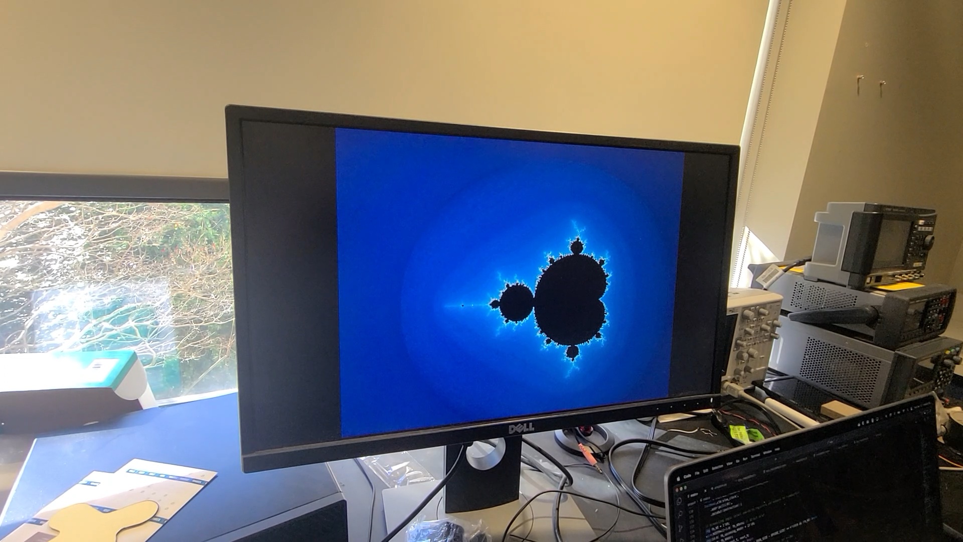 A monitor displaying a zoomed-out rendering of the Mandelbrot set.