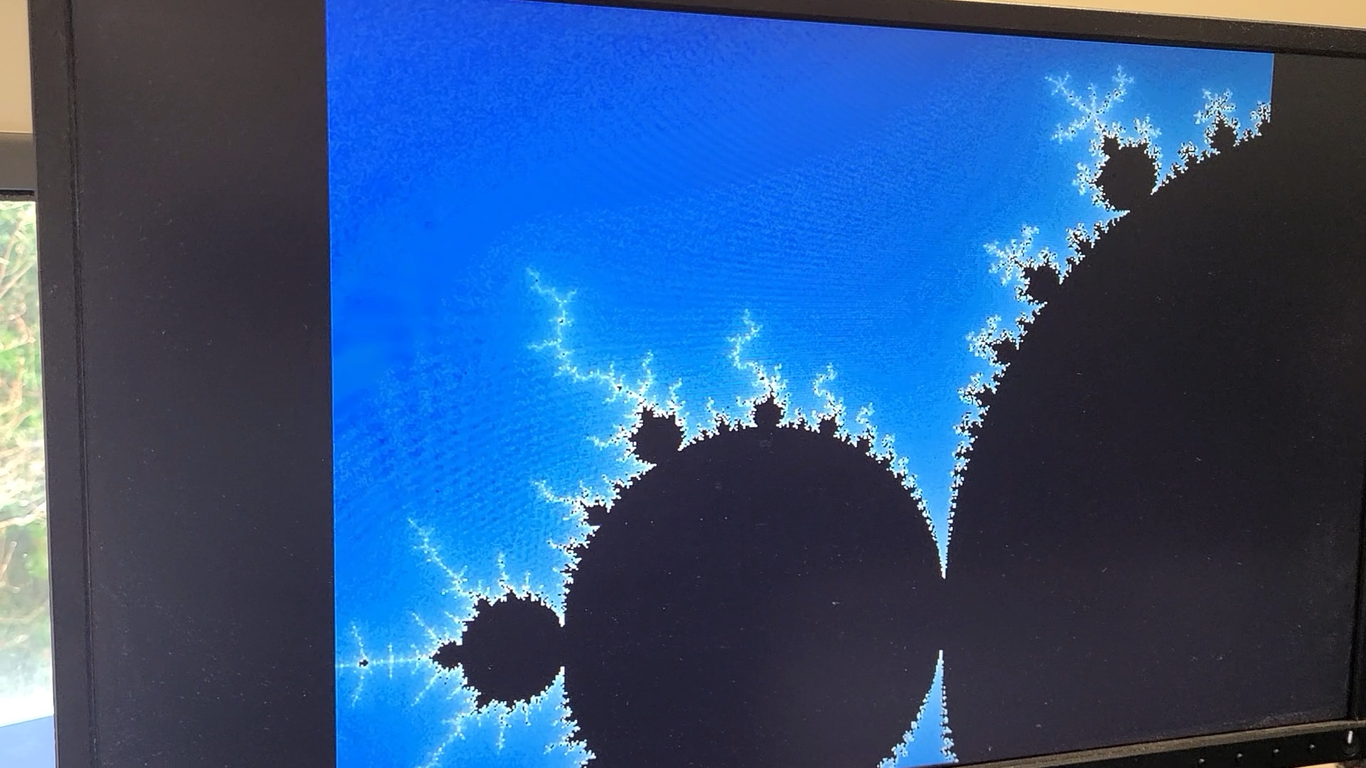 A monitor displaying a zoomed-in rendering of the Mandelbrot set.